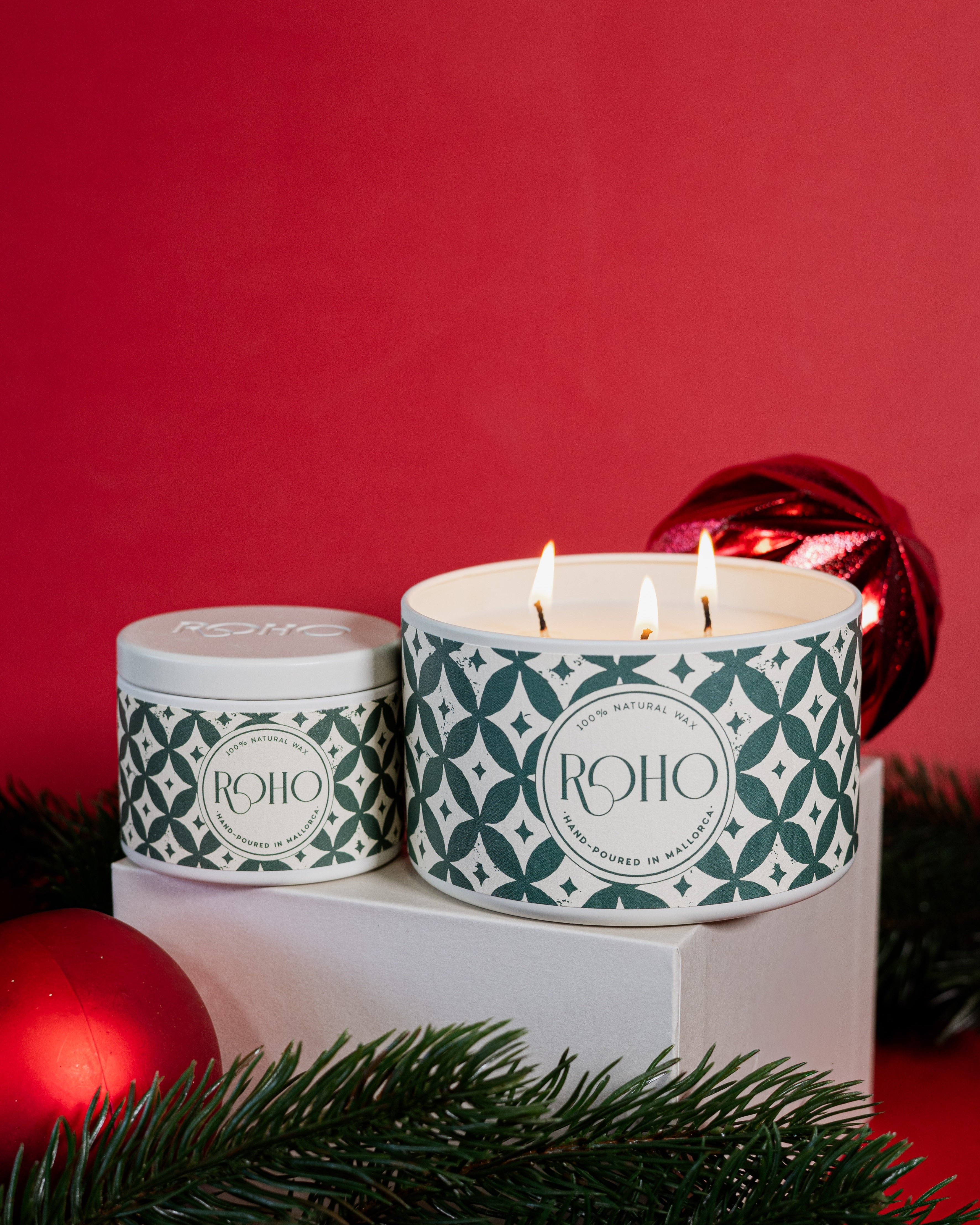 Two scented candles with green patterns on a white base against a red background. Orange and Cinnamon Scent. Gift Idea