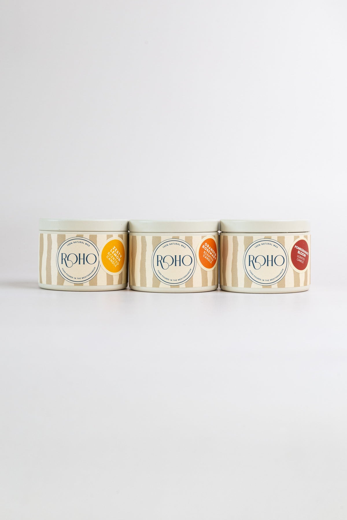 Three ROHO 90g candles in beige tins side by side – Zesty Lemon, Orange & Rosemary and Pomegranate Bloom