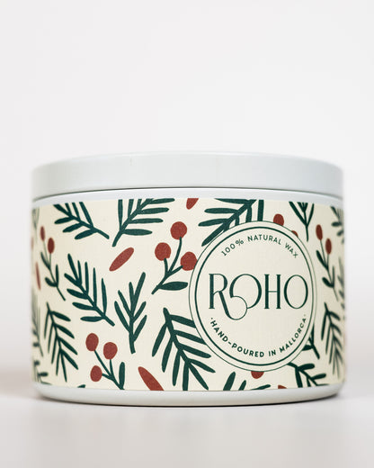 Candle with decorative winter / Christmas label featuring green leaves and red berries on a white background, 