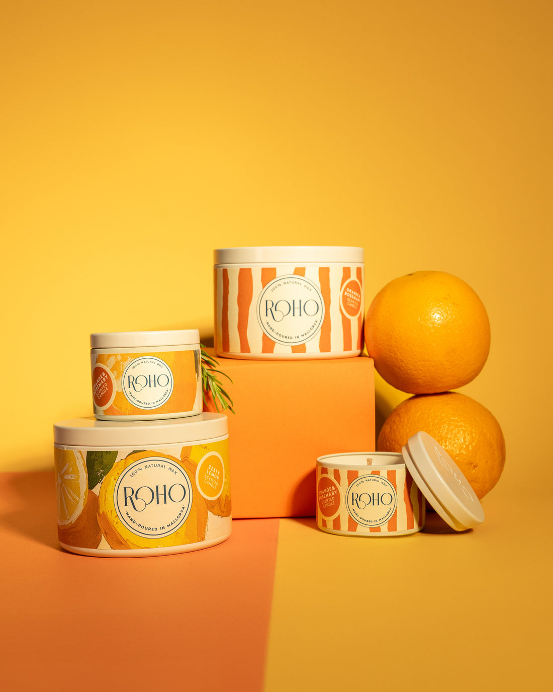Candle containers with orange design and ROHO branding on a yellow background, scent: Orange &amp; Rosemary