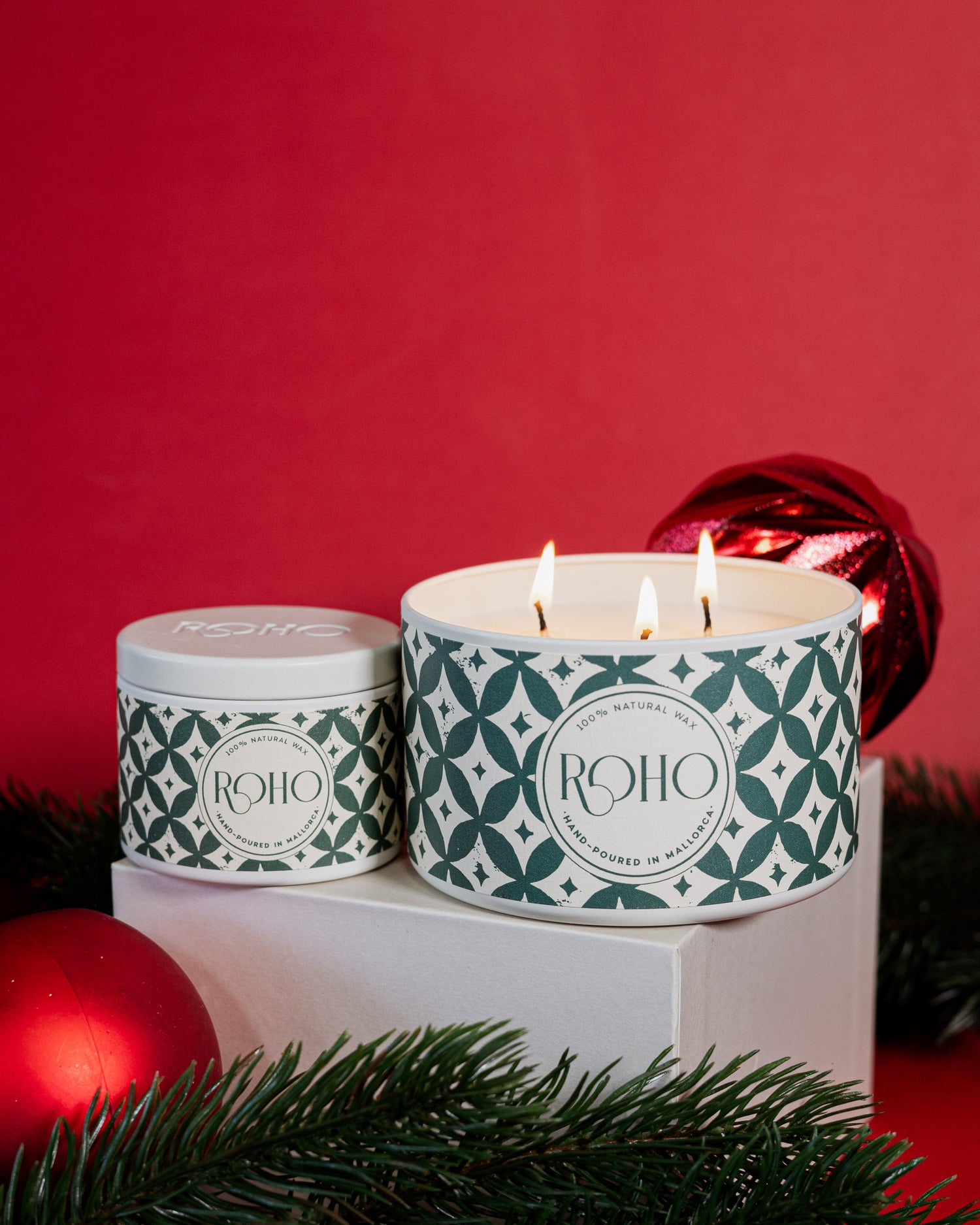 Two scented candles with green patterns on a white base against a red background. Orange and Cinnamon Scent. Gift Idea