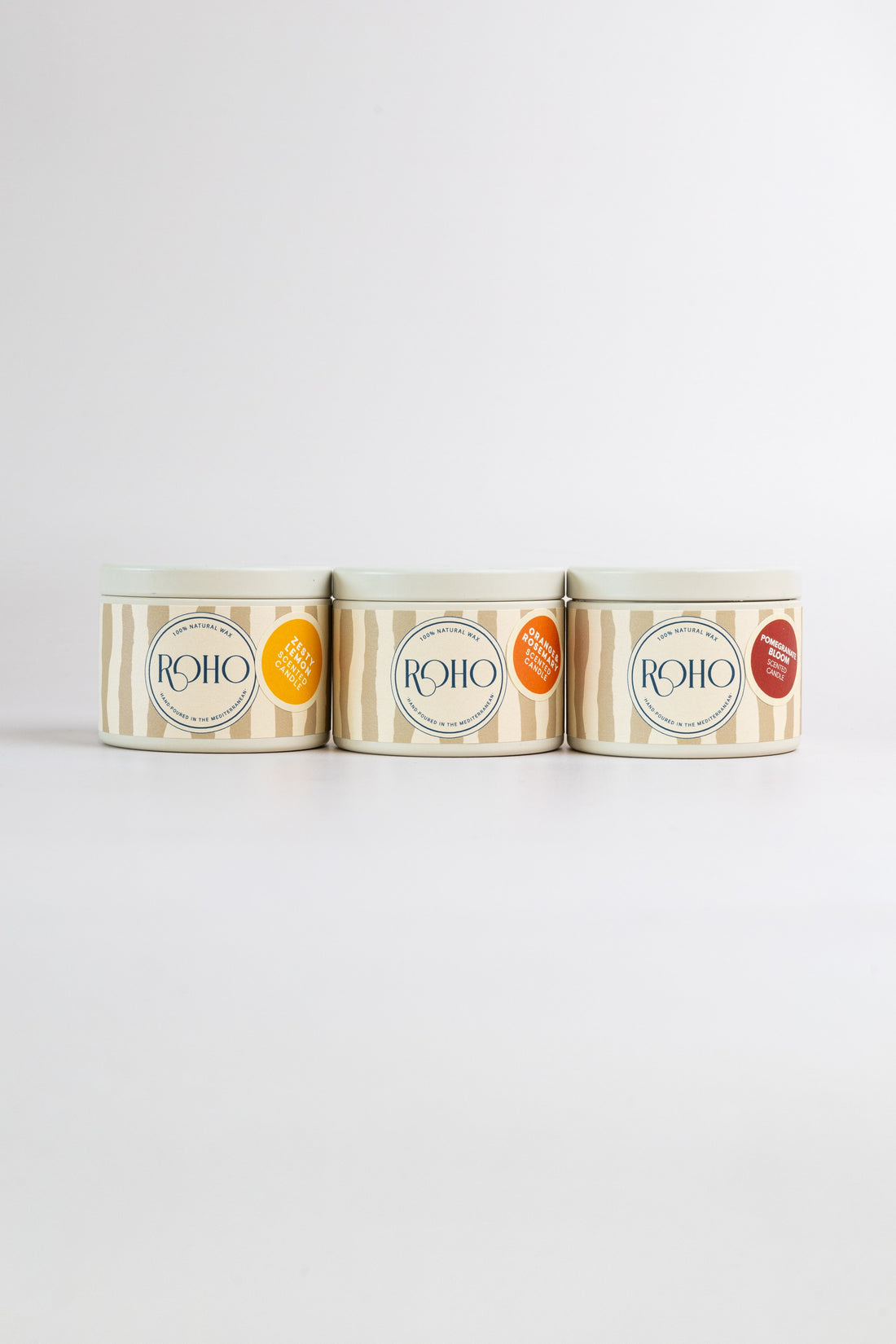 Three ROHO 90g candles in beige tins side by side – Zesty Lemon, Orange &amp; Rosemary and Pomegranate Bloom